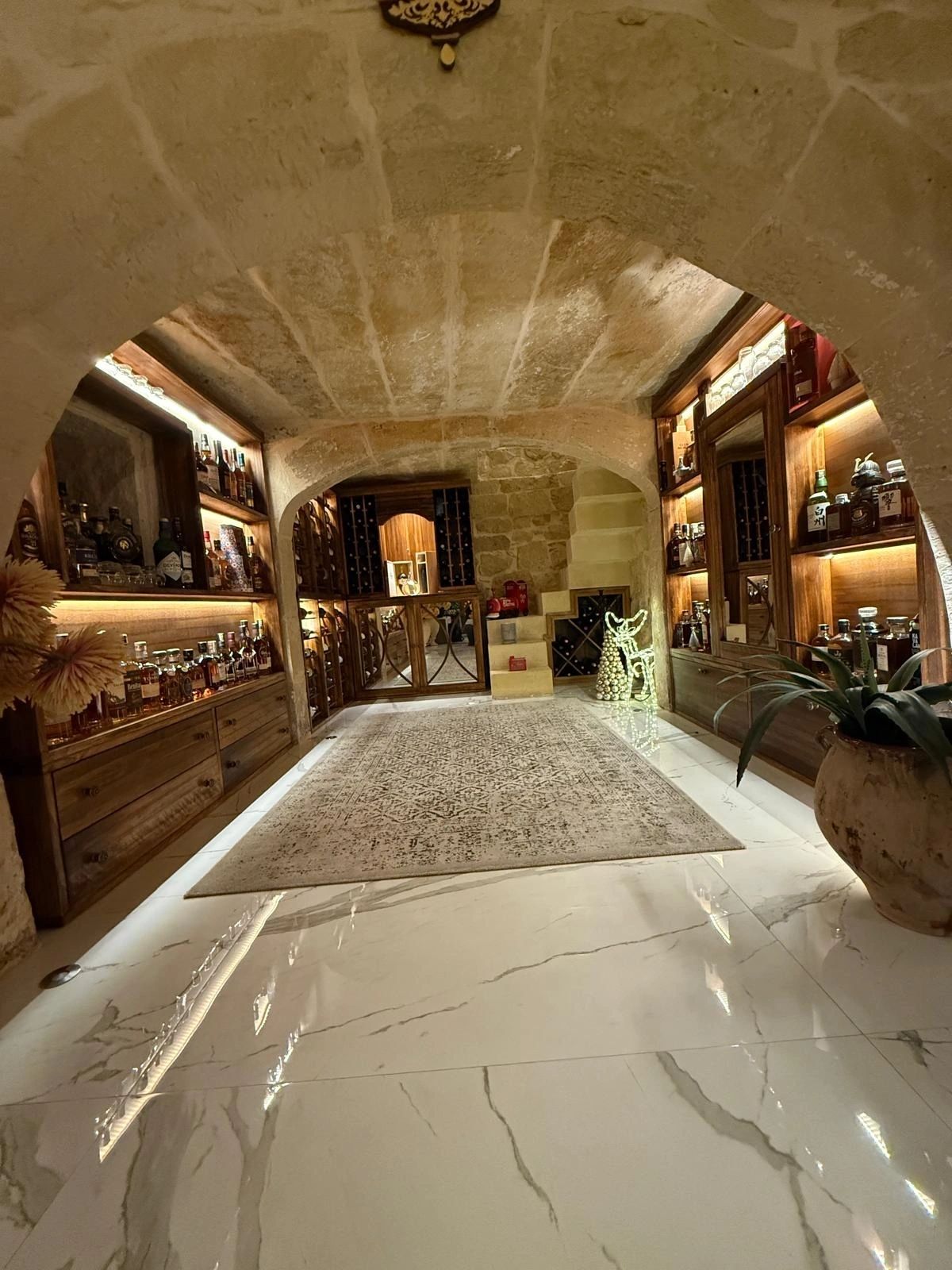 Vaulted stone wine and whiskey cellar with backlit timber shelving